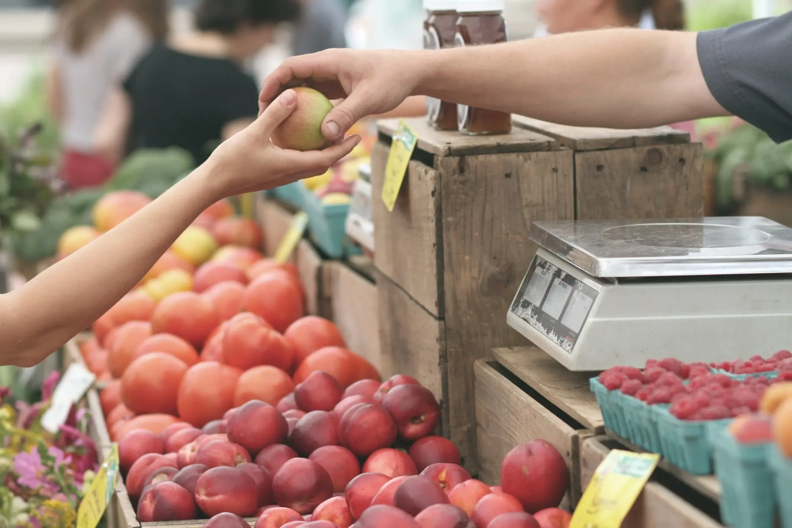 Marktstand mit frischem Obst und Gemüse – ein Kunde nimmt einen Apfel entgegen
